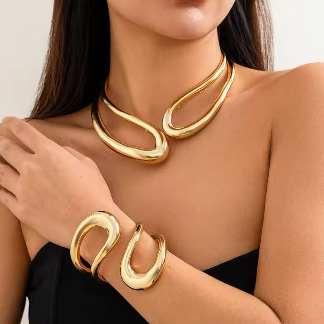 Komplettes Metallic Schmuckset bestehend aus Halskette und Armband, getragen von einer Frau. Beide Teile in goldfarbenem Metall mit robustem, modernem Design, ideal für alltägliche Looks und besondere Anlässe. Das Set zeigt eine verstellbare Halskette und ein flexibles Armband.