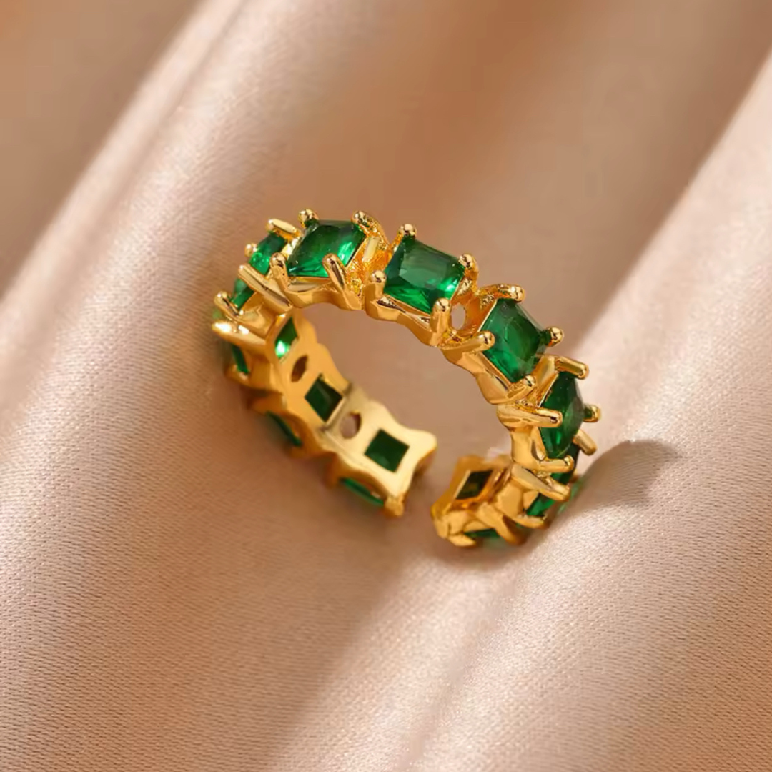 Ring Elegance mit grünen Steinen, auf einem goldenen Seidentuch präsentiert. Der stilvolle, mehrschichtige Ring aus hochwertigem Edelstahl in Goldfarbe bietet ein elegantes Design, ist größenverstellbar und sorgt für ein luxuriöses Erscheinungsbild.