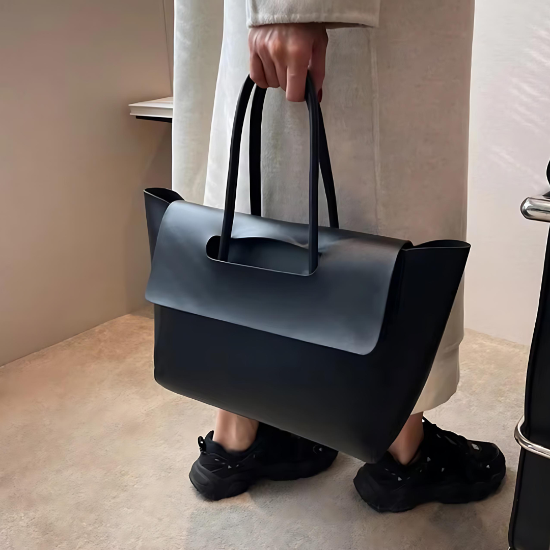 Frau hält den Vintage Shopper in Farbe Schwarz an den Schulterriemen – Die stilvolle Tasche aus hochwertigem PU-Material zeigt sich im Vintage-Design. Die Schulterriemen bieten Stabilität und Komfort, ideal für den täglichen Gebrauch und besondere Anlässe. Der Fokus liegt auf der eleganten und funktionalen Handhabung der Tasche.