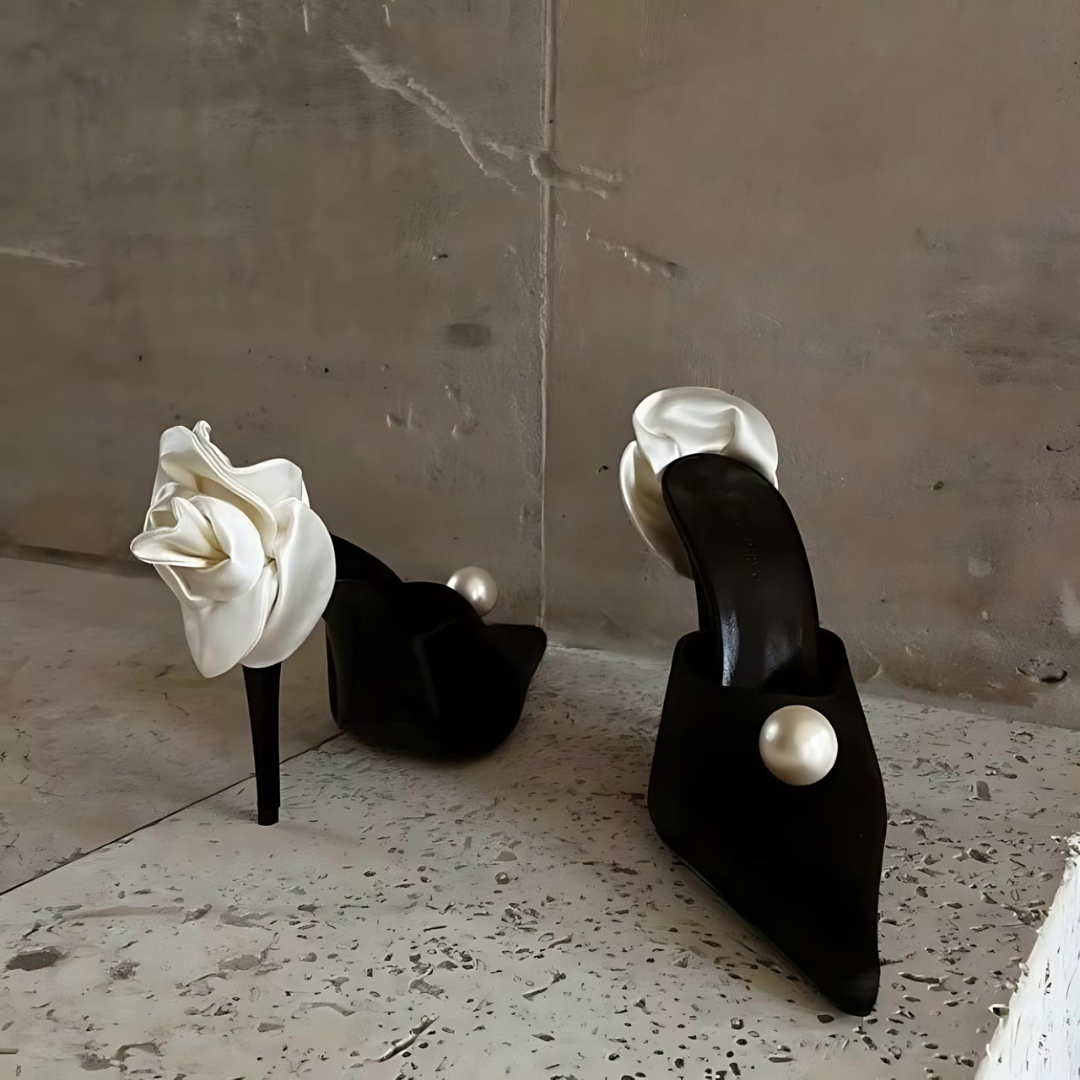 Vorder- und Rückansicht der Pearl Blossom Heels auf einer Treppe. Die eleganten Stilettos mit spitzer Zehenpartie, Satin-Obermaterial und zarten Perlen- sowie Blumenapplikationen präsentieren sich mit einem Slingback-Riemen und hohem Absatz für einen glamourösen Look.