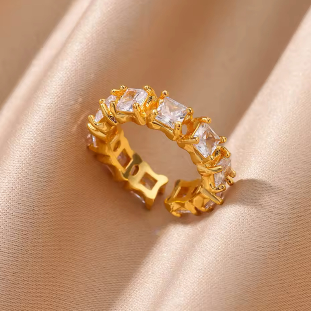 Ring Elegance mit weißen Steinen, auf einem goldenen Seidentuch präsentiert. Der elegante, mehrschichtige Ring aus hochwertigem Edelstahl in Goldfarbe zeichnet sich durch sein luxuriöses Design und die verstellbare Größe aus, ideal für besondere Anlässe