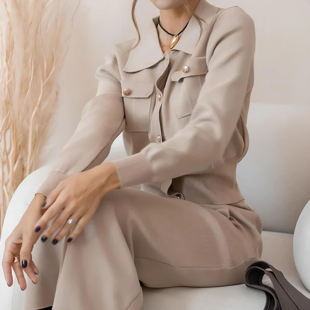 Sitzende Frau in elegantem Set Celly in Khaki, bestehend aus einem Strick-Blazer und einem passenden Rock. Das Vintage-inspirierte 2-teilige Set bietet eine feminine Silhouette und höchsten Tragekomfort, ideal für Büro, Freizeit und besondere Anlässe in der Herbst- und Wintersaison. Der weiche, hochwertige Strickstoff sorgt für zusätzlichen Luxus und Wärme.