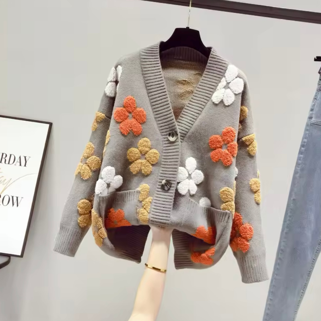 Produktfoto des eleganten Cardigans Flowers in Grau, in Vorderansicht. Der Cardigan zeigt sich im lockeren, westlichen Stil mit langem Ärmel und femininen V-Ausschnitt, gefertigt aus weichem, hochwertigem Strickmaterial. Die entspannte Passform bietet Komfort und Wärme für die Herbstsaison und verleiht jedem Outfit eine herbstliche Eleganz.