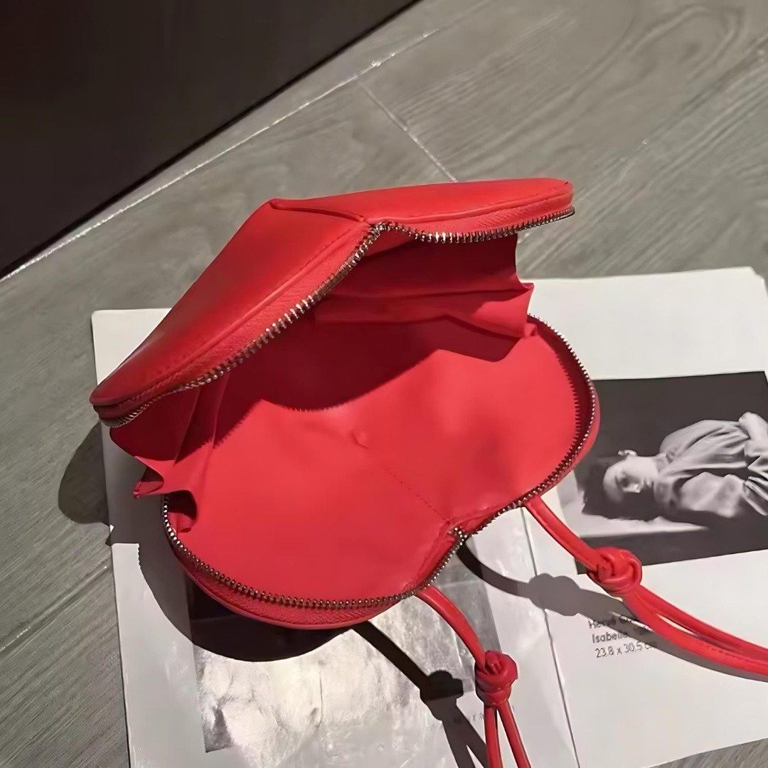 Rote Herz-Tasche aufgeklappt auf einem Tisch liegend. Die Tasche zeigt ihre herzförmige Silhouette und das geräumige Innenfach, ideal für die Aufbewahrung von Essentials. Das Bild hebt die elegante und funktionale Gestaltung der Tasche hervor.
