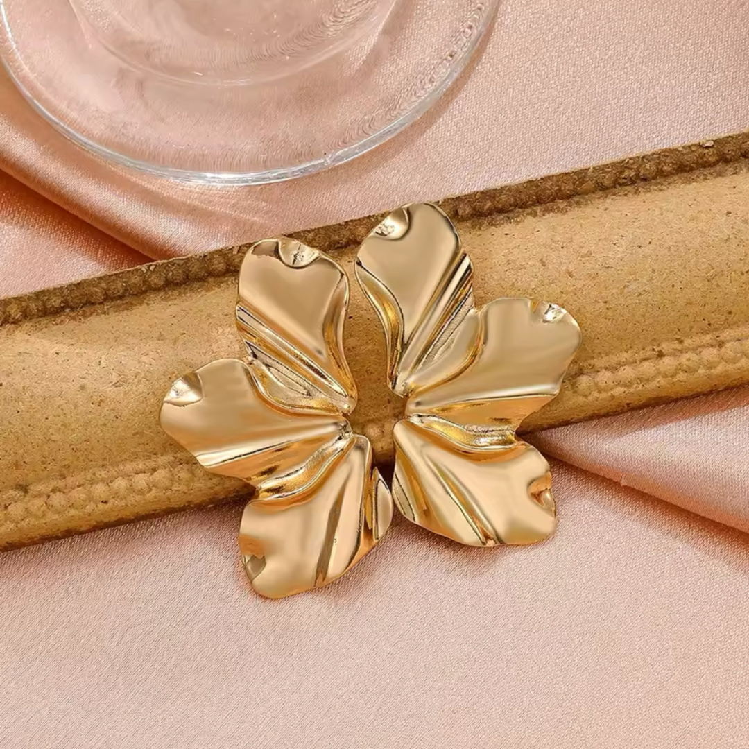 Goldfarbene Ohrstecker im Blütenblatt-Design auf neutralem Hintergrund. Die filigranen Ohrringe zeichnen sich durch eine glänzende Oberfläche aus und bieten einen eleganten und trendigen Look.