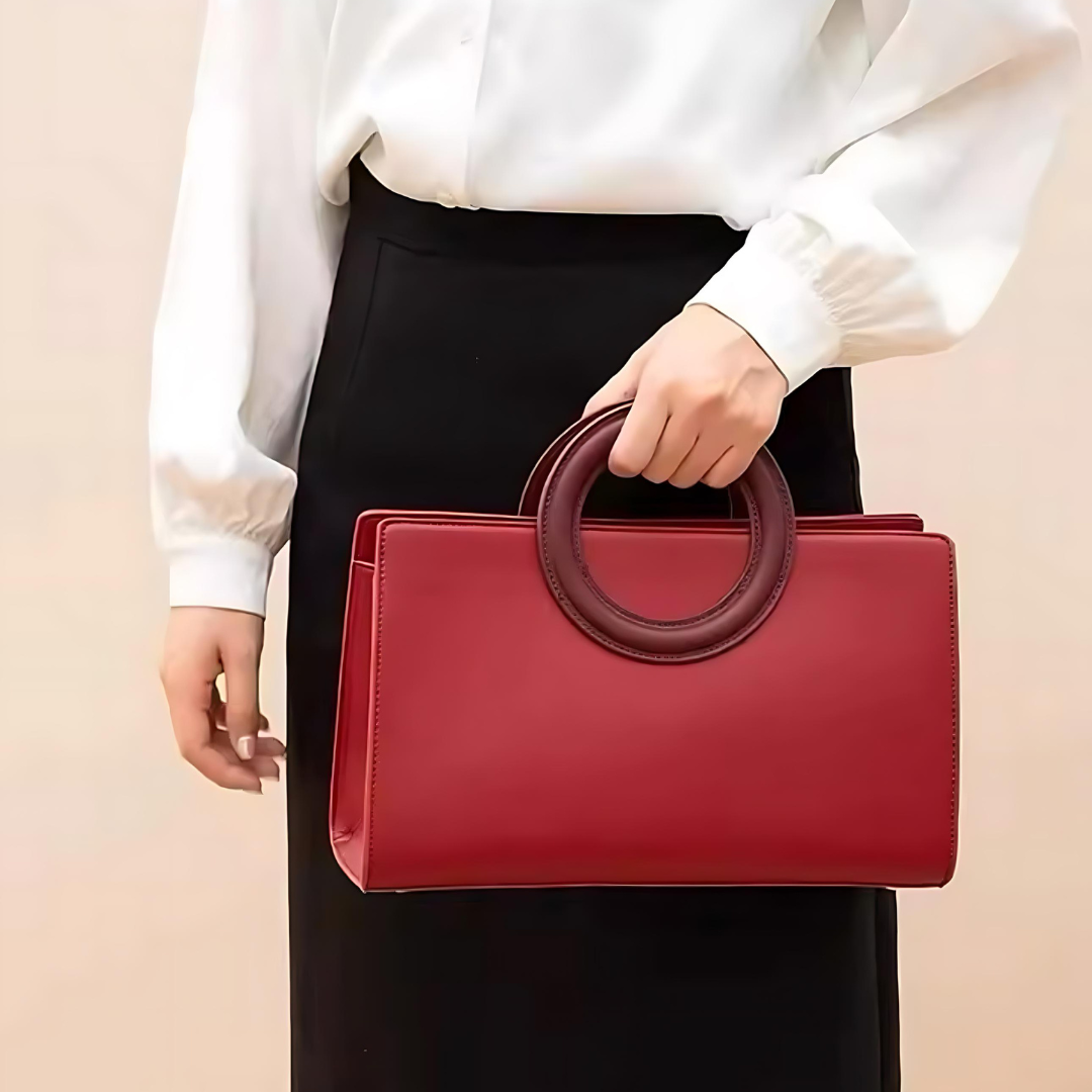 Die Tasche Ruby aus hochwertigem strukturiertem Leder in auffälligem Rot, getragen von einer Frau. Die Handtasche wird als Schulter- oder Umhängetasche präsentiert und ergänzt das Outfit der Frau mit ihrer luxuriösen Note. Die Tasche ist elegant über der Schulter oder umgehängt und ideal für besondere Anlässe wie Hochzeiten oder Events.