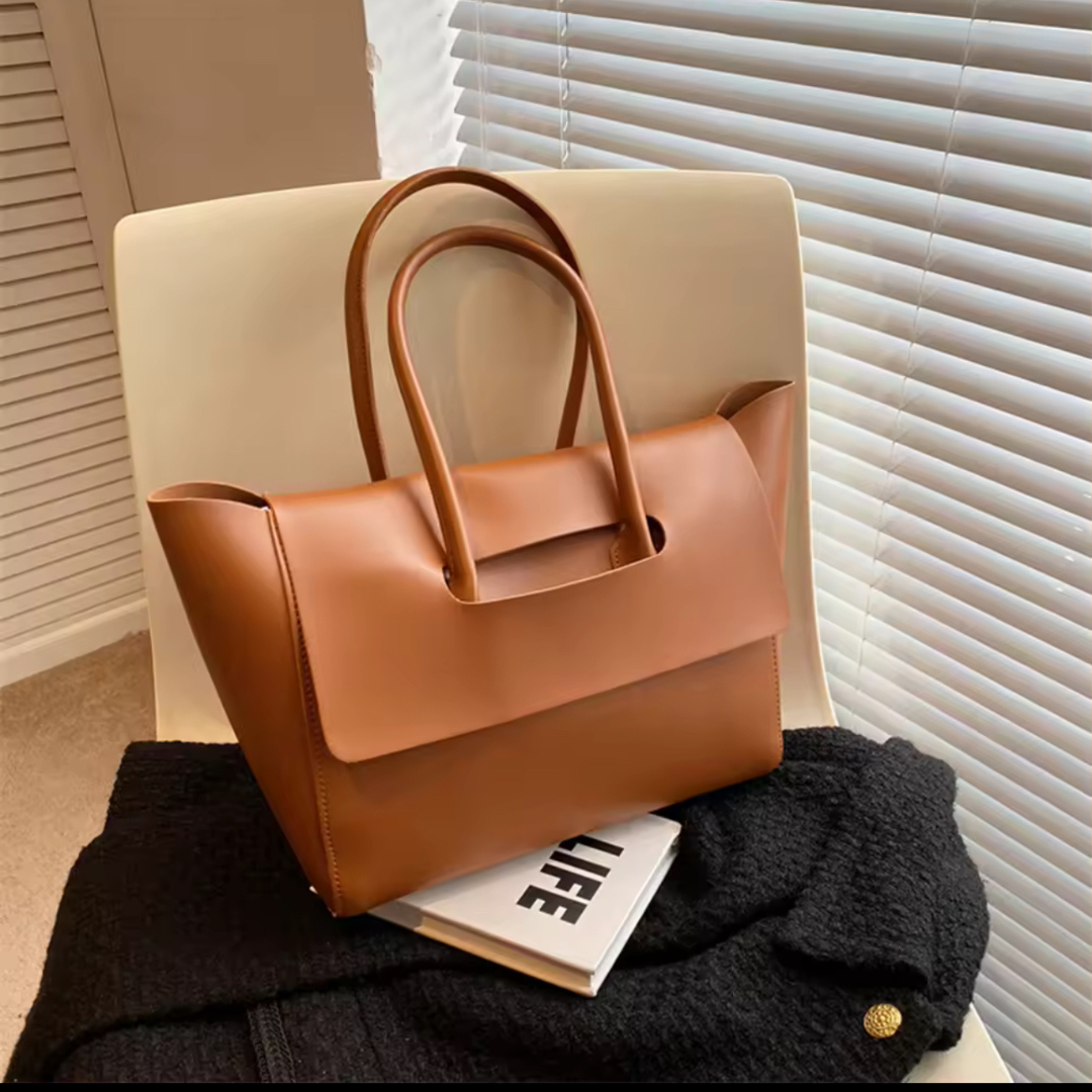 Vintage Shopper in Farbe Braun auf einem Stuhl – Die stilvolle Tasche aus hochwertigem PU-Material steht auf einem Stuhl, was ihr elegantes, klassisches Design und die vielseitige Verwendbarkeit betont. Ideal für den Alltag oder besondere Anlässe, kombiniert diese Tasche Vintage-Charme mit modernem Komfort.