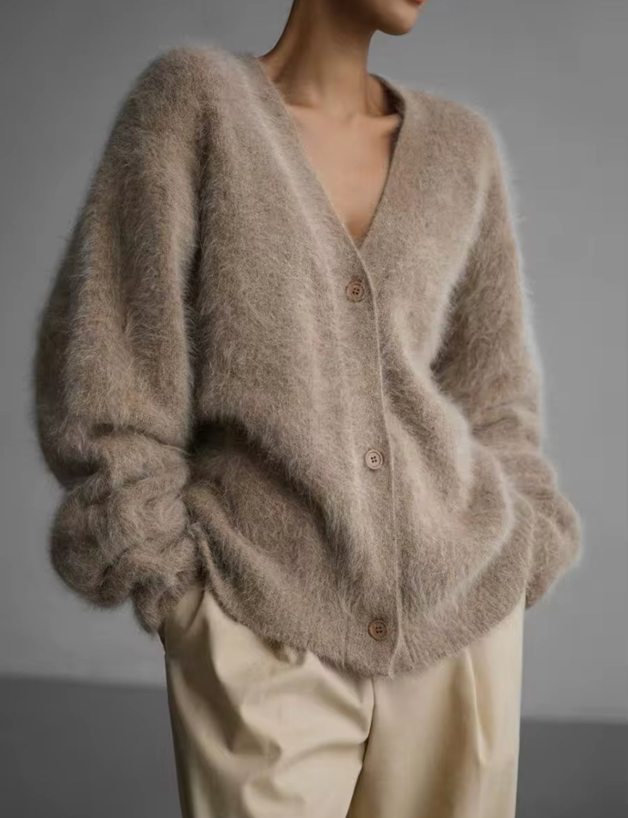 Frau trägt die elegante Strickjacke Autumn Grace in Khaki in Vorderansicht. Die Strickjacke zeichnet sich durch ihr modernes, einreihiges Design und die langen Ärmel aus, gefertigt aus weicher, flexibler Strickqualität. Der lockere, lässige Schnitt bietet Komfort und Wärme, ideal für die Herbst- und Wintersaison. Diese Strickjacke kombiniert klassischen Chic mit zeitgemäßem Stil, perfekt für Alltag und besondere Anlässe.