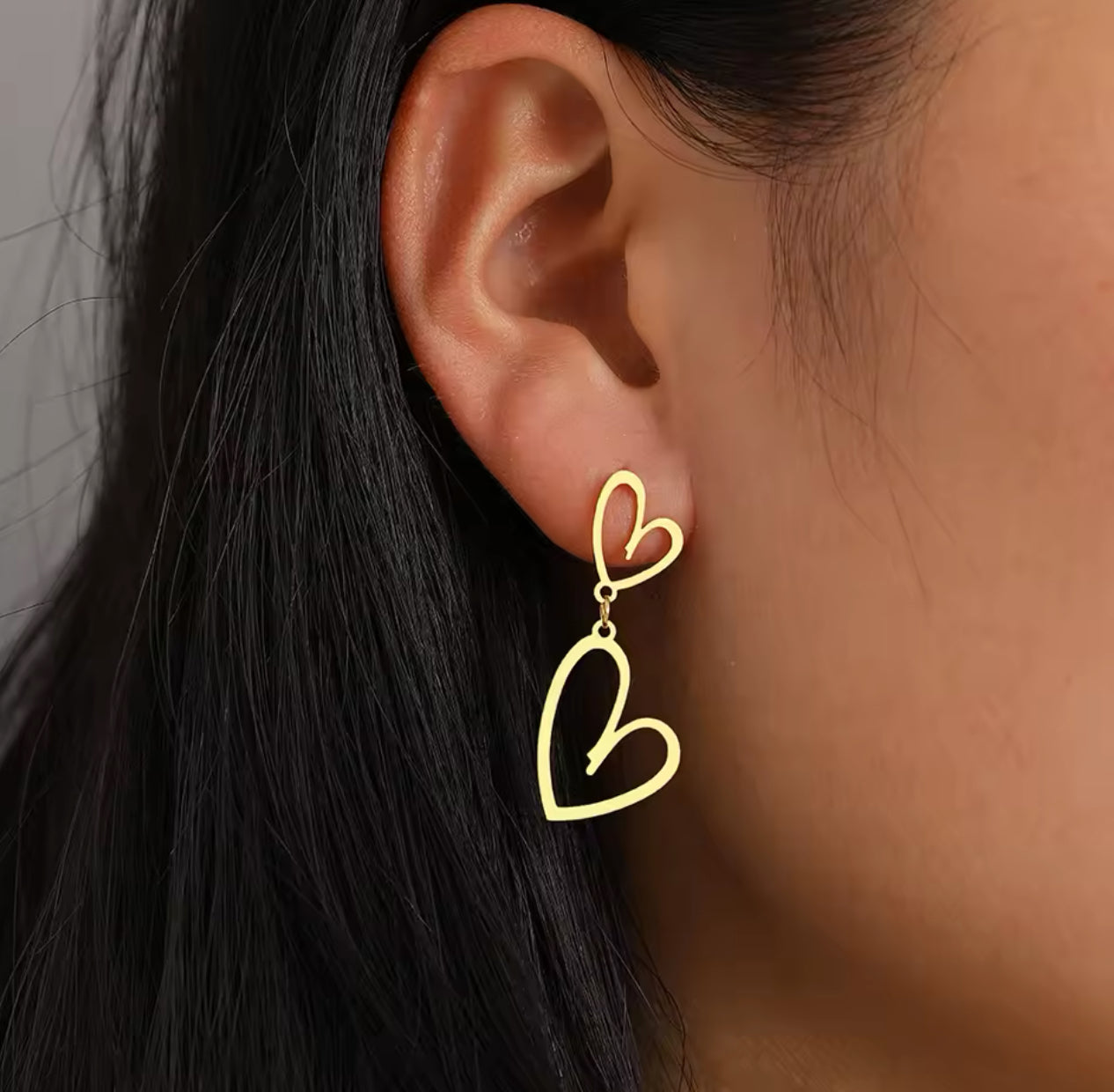 Nahaufnahme von Ohrsteckern Golden Heart, getragen von einer Frau. Die eleganten Gold-Ohrstecker aus hochwertigem Edelstahl zeigen charmante Herzanhänger und verleihen jedem Outfit einen luxuriösen Glanz. Ideal für besondere Anlässe oder als stilvolles Alltagsaccessoire.