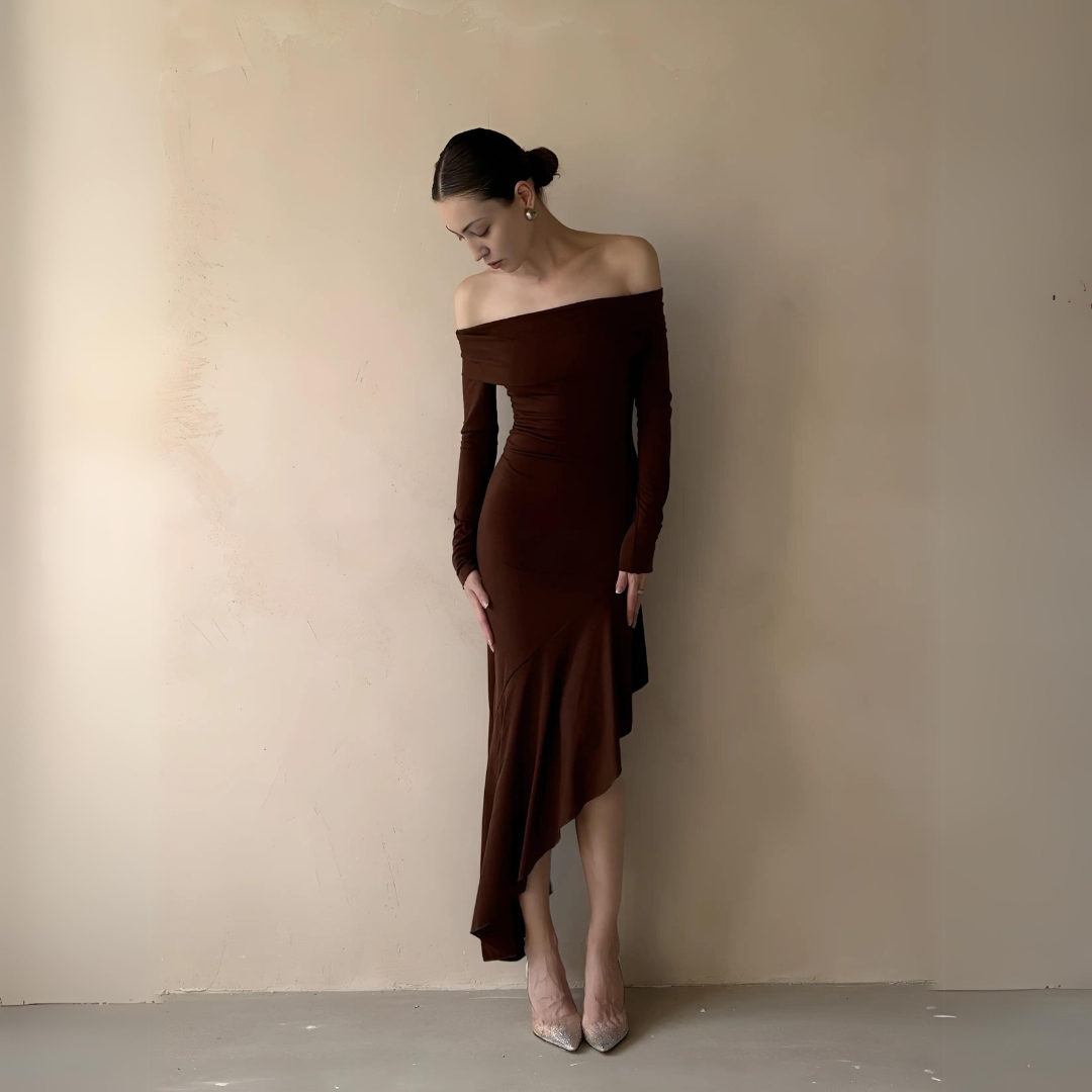 Frau in elegantem Maxikleid Joanna in Frontansicht. Das Kleid hat einen figurbetonten Bodycon-Schnitt, Slash-Neck-Ausschnitt und lange Ärmel. Es zeichnet sich durch stilvolle Rüschen und ein asymmetrisches Design aus, ideal für besondere Anlässe wie Hochzeiten und Partys.